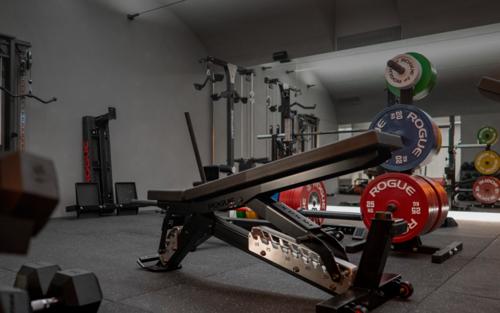 Modern gym inside PoW.space coworking space in Lugano, featuring Rogue fitness equipment, weightlifting bench, and colorful weight plates, promoting work-life balance and wellbeing.